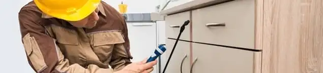 Roach exterminator applying treatment under kitchen cabinets in Lakeland, FL