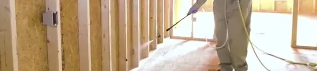 Termite treatment technician applying spray along framing and unfinished walls in Lakeland, FL
