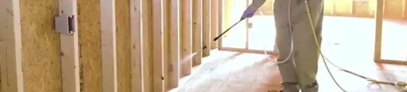 Termite treatment technician applying spray along framing and unfinished walls in Lakeland, FL